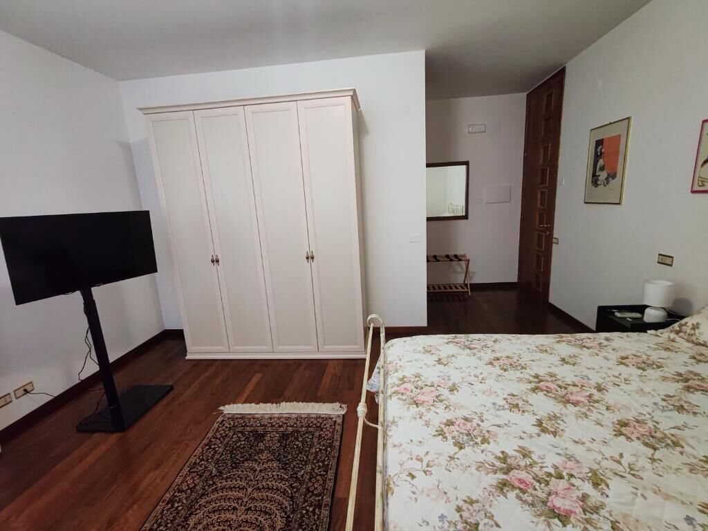 Une chambre à coucher avec un lit, une armoire, un téléviseur, un tapis, et une salle de bain visible au fond.