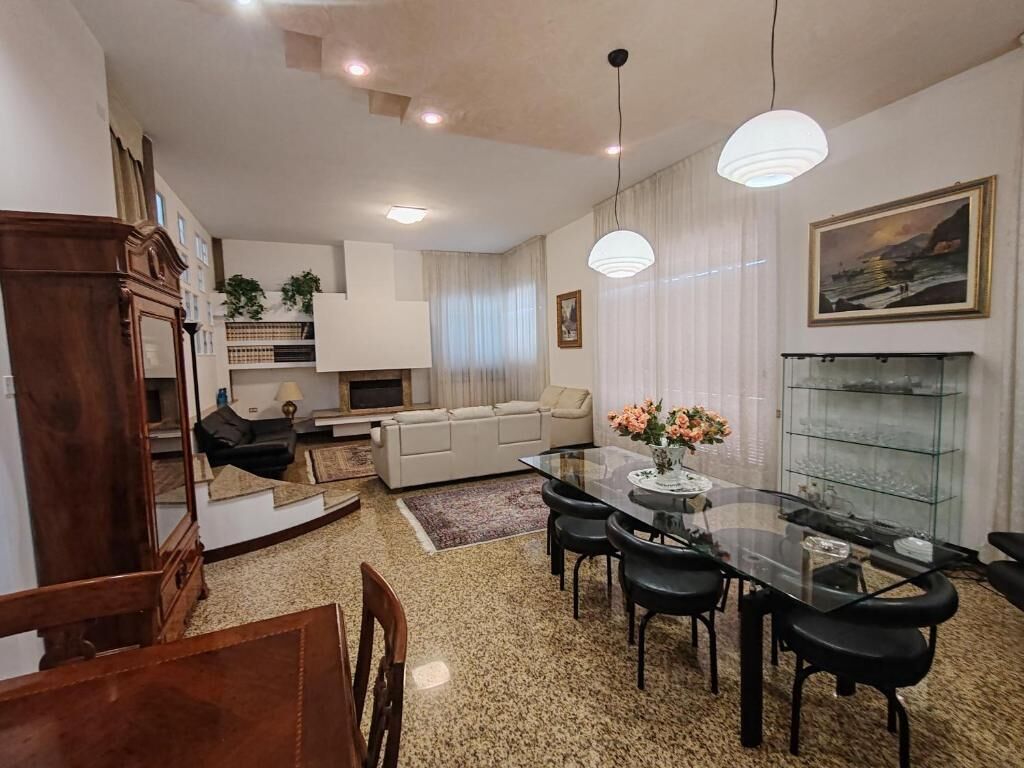 A dining area with a glass table and chairs, a sofa, a fireplace, and a painting on the wall.
