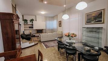 A dining area with a glass table and chairs, a sofa, a fireplace, and a painting on the wall.