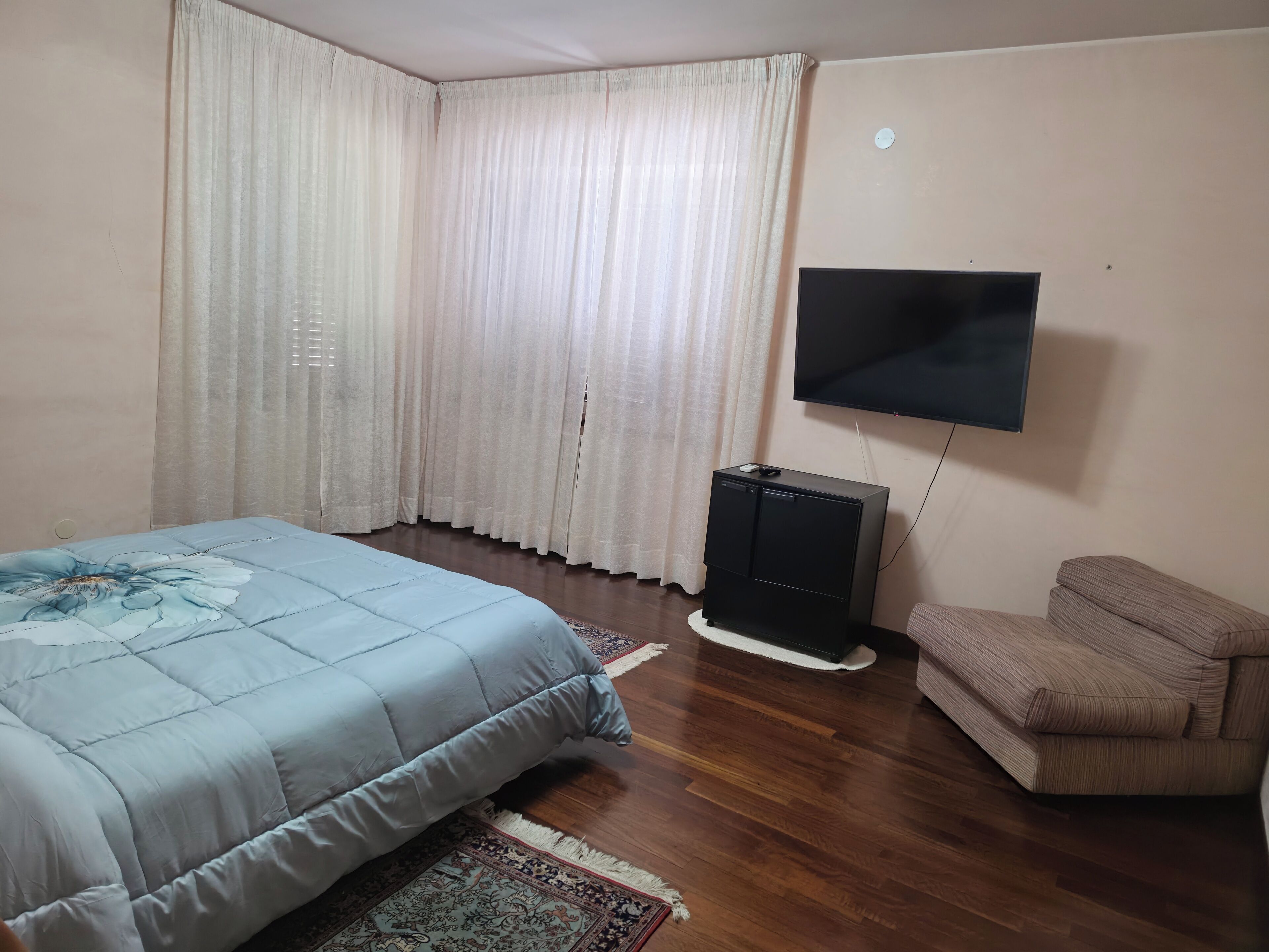 A bedroom with a bed, a TV, a sofa, and a window with curtains.