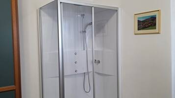 A glass-enclosed shower room with a wooden floor, white walls, and a framed picture on the wall.