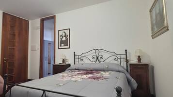 A bedroom with a bed, a wooden door, a nightstand, a lamp, a framed picture, and a patterned rug.