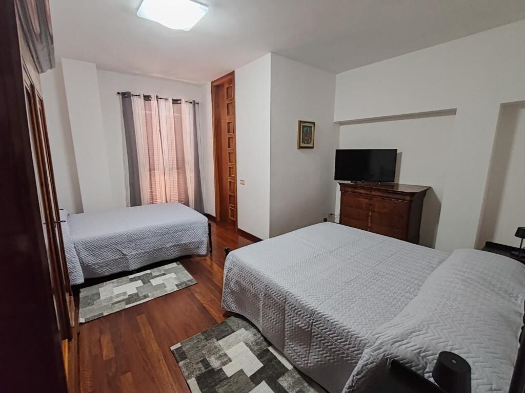 Ein Schlafzimmer mit zwei Betten, einem Fernseher auf einem Holzkasten und einer Tür zu einem anderen Raum.