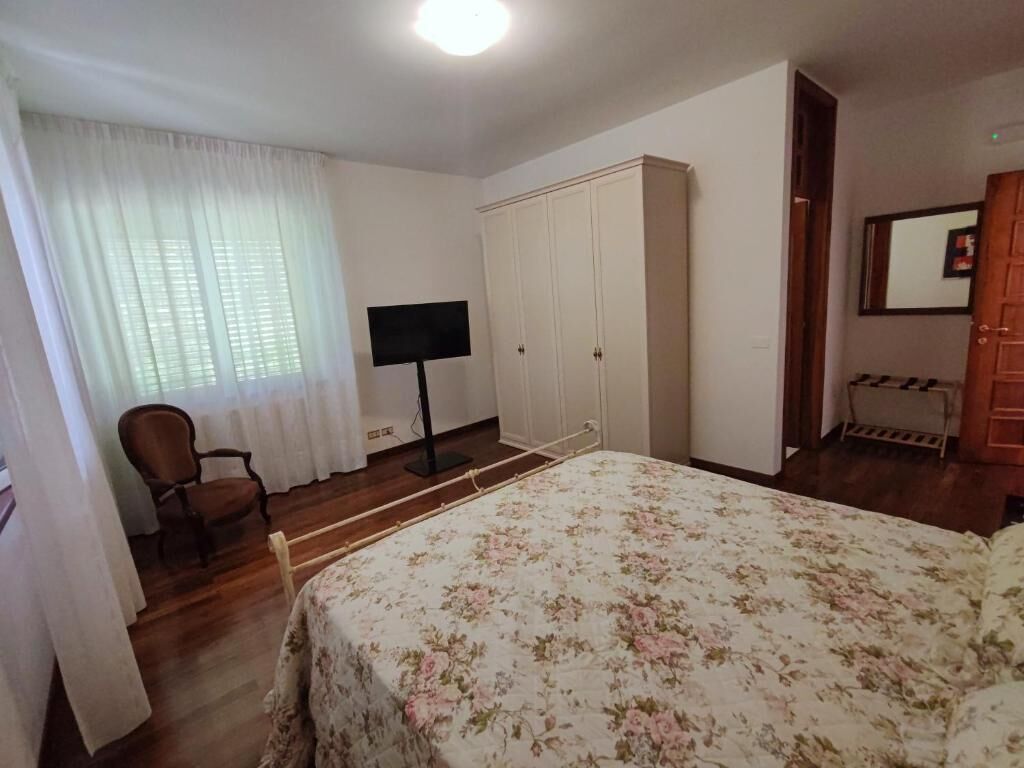 Una camera da letto con un letto, una sedia, un armadio, una televisione e uno specchio.