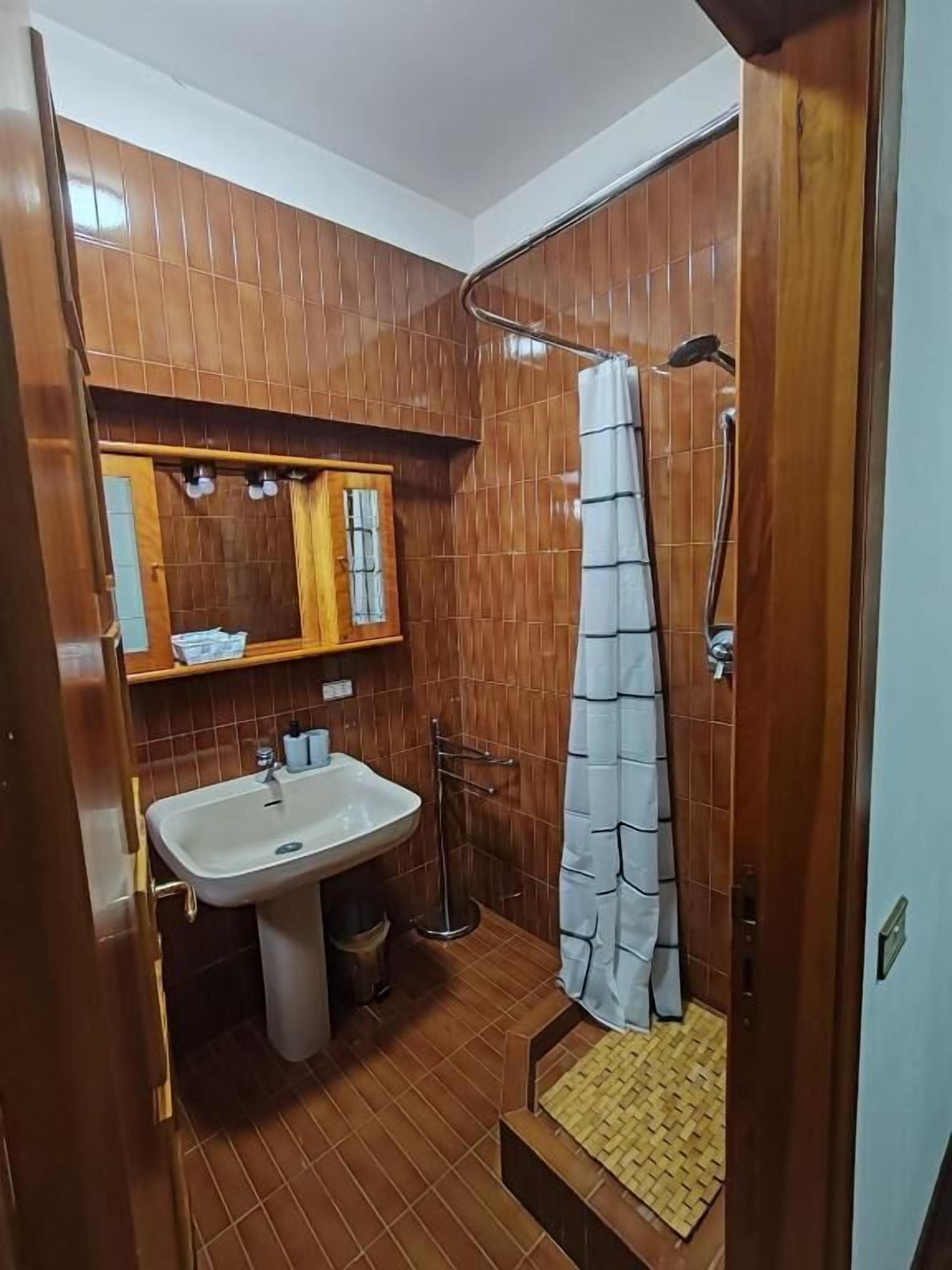 Une salle de bain avec un plancher en bois, un lavabo, un miroir et un espace douche.