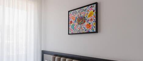 Habitación de hotel con cama, cabecero, ventana con cortinas y una obra de arte enmarcada en la pared.