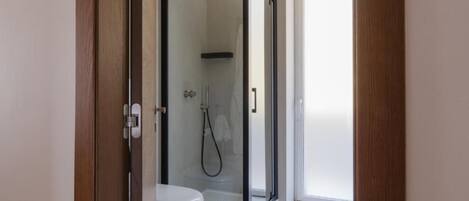 A modern bathroom with a glass-enclosed shower, a white toilet, and a door leading to a bright room.