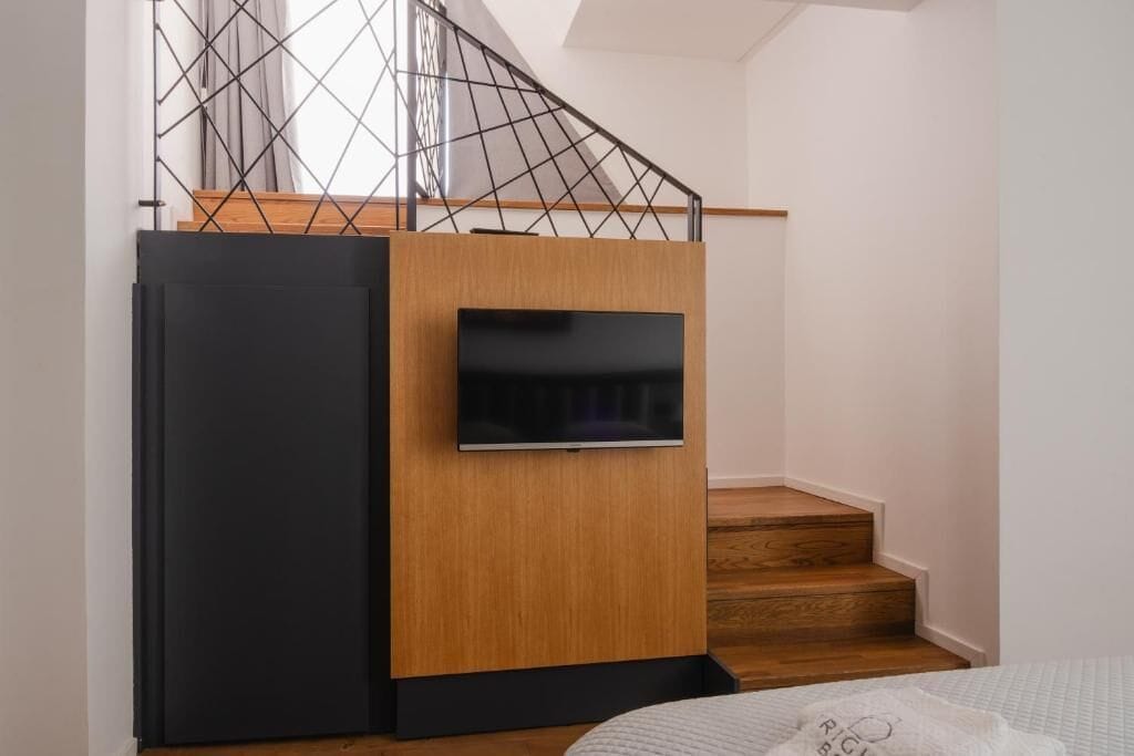 A modern staircase with a TV screen, wooden steps, and a geometric railing.