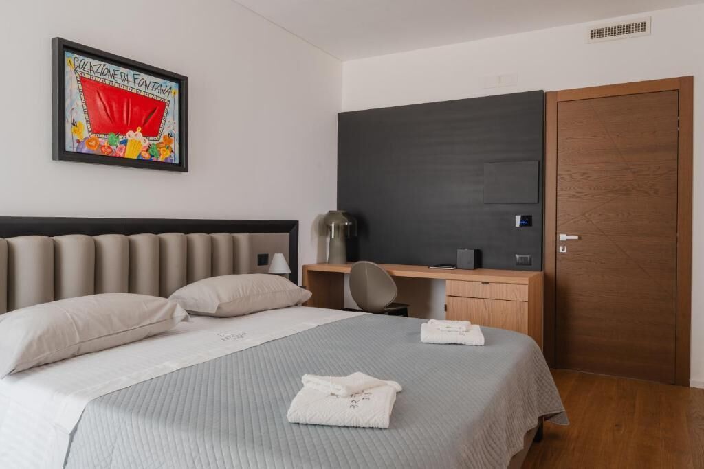 Habitació d'hotel amb llit, escriptori, cadira, armari i un quadre al mur.