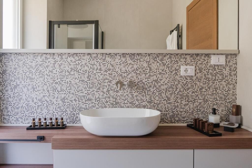Een badkamer met een witte wasbak, een betegelde spatwand en een houten aanrechtblad.