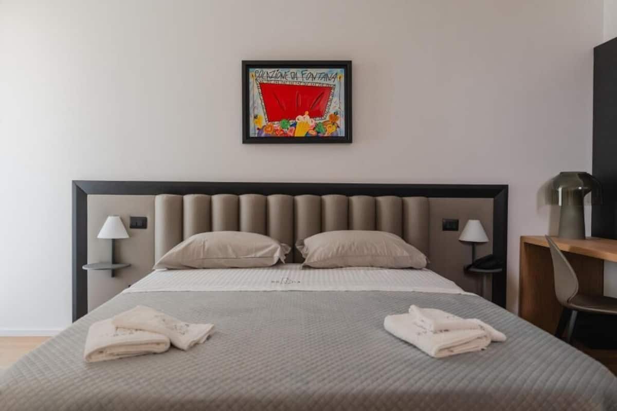 A neatly made bed with two pillows, a bedside table with a lamp, and a framed picture on the wall.