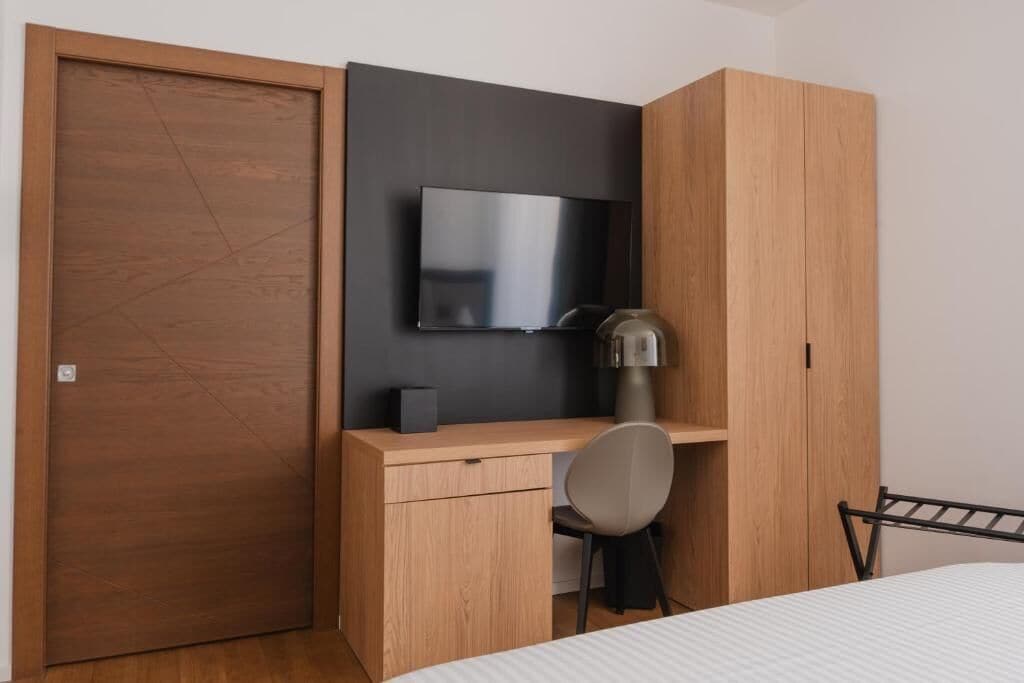 A bedroom with a bed, a desk with a chair, a TV, and a wardrobe.
