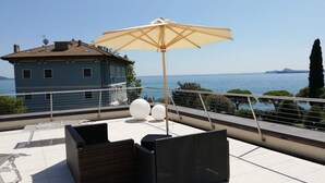 Eine Dachterrasse mit Korbmöbeln, einem großen Sonnenschirm und Blick auf das Meer.