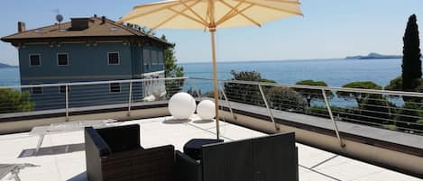 A rooftop terrace with wicker furniture, a large umbrella, and a view of the sea.