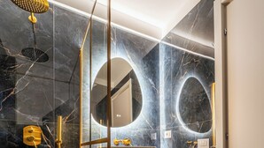 Ein modernes Badezimmer mit Glastrennwand, goldenen Armaturen und einem Marmorboden.