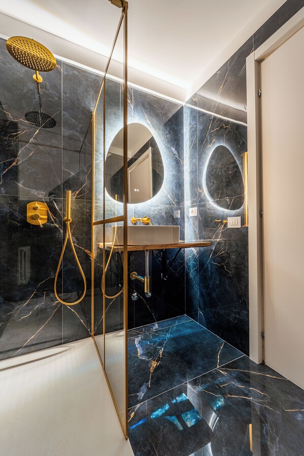 A modern bathroom with a glass partition, gold fixtures, and a marble floor. - Giulia Urban Retreat Suites (Rome)