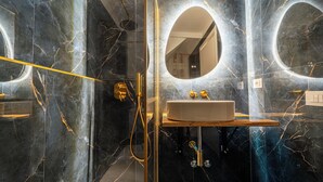 Ein modernes Badezimmer mit Marmorwand, einem runden Spiegel, einem Waschbecken mit goldfarbenen Armaturen und einer Duschkabine.