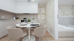 Een moderne keuken met witte kasten, een eettafel gedekt voor vier personen, en een bed in de aangrenzende kamer.