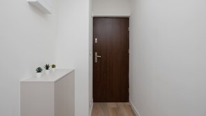 Een smalle gang met een houten deur, witte muren en een klein kastje met plantenpotten.