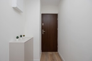 Ein schmaler Korridor mit einer Holztür, weißen Wänden und einer kleinen Vitrine mit Topfpflanzen.