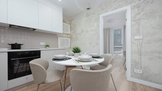 Een moderne keuken met witte kasten, een inbouwoven en een eethoek met een ronde tafel en vier stoelen.