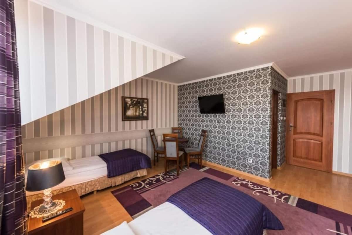 A bedroom with a bed, a desk, a chair, a TV, and a door.