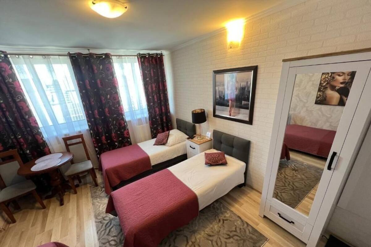 A hotel room with two beds, a small table, a chair, a lamp, and a door with a mirror.