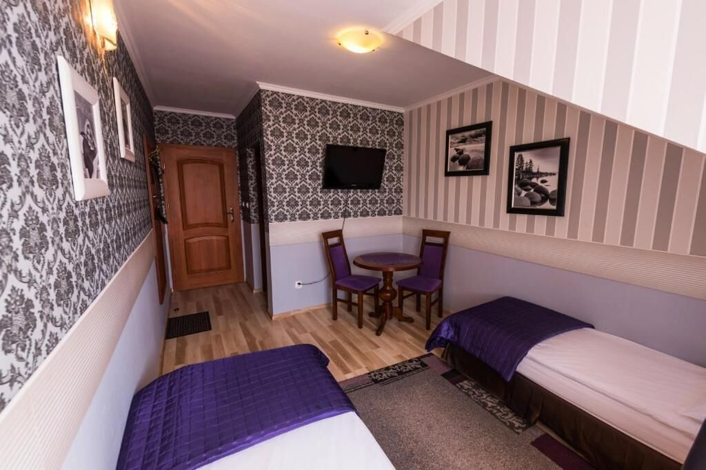 A compact room with two beds, a small table, and a TV mounted on the wall.