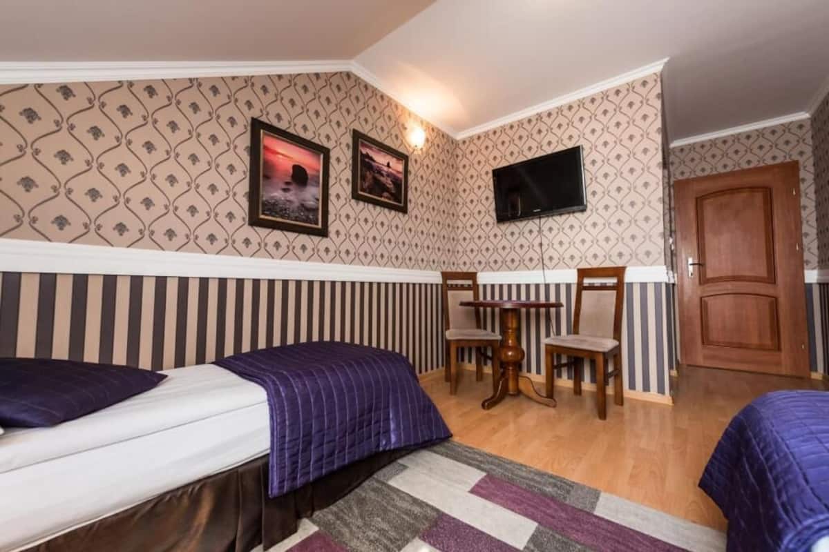 A room with two beds, a TV, a wooden door, and a patterned wall.