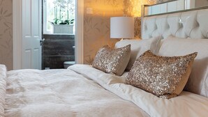 Ein Schlafzimmer mit einem Bett, Zierkissen, einem Nachttisch, einer Lampe und einem Fenster mit Blick ins Freie.