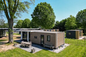 Une maison mobile moderne dotée d’un patio, d’une table à manger et d’un banc.