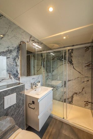 A modern bathroom with a marble wall, a glass shower enclosure, and a white vanity. - Lessenaar 21 | sfeervol 4 persoons chalet in Zennewijnen (Zennewijnen)