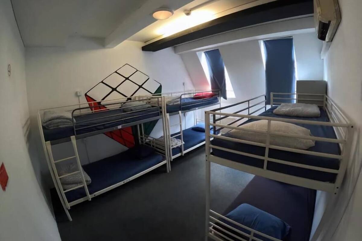 Une chambre de dortoir avec des lits superposés, un ventilateur de plafond et une fenêtre avec des rideaux.