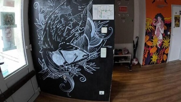 Een kamer met een zwarte muur, waarop een illustratie van een witte vogel staat, een whiteboard en een deur met een raam.