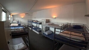 Een slaapzaal met stapelbedden in rijen, elk met een kussen en een klein nachtkastje.