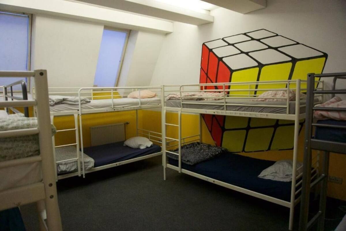 Une chambre de dortoir avec des lits superposés, une fenêtre et une fresque représentant un Rubik's Cube sur le mur.