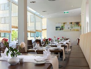 A restaurant with long tables, white tablecloths, and vases with flowers. - Sunday Hotel Saarbruecken Sued Triple Room (Saarbrücken)