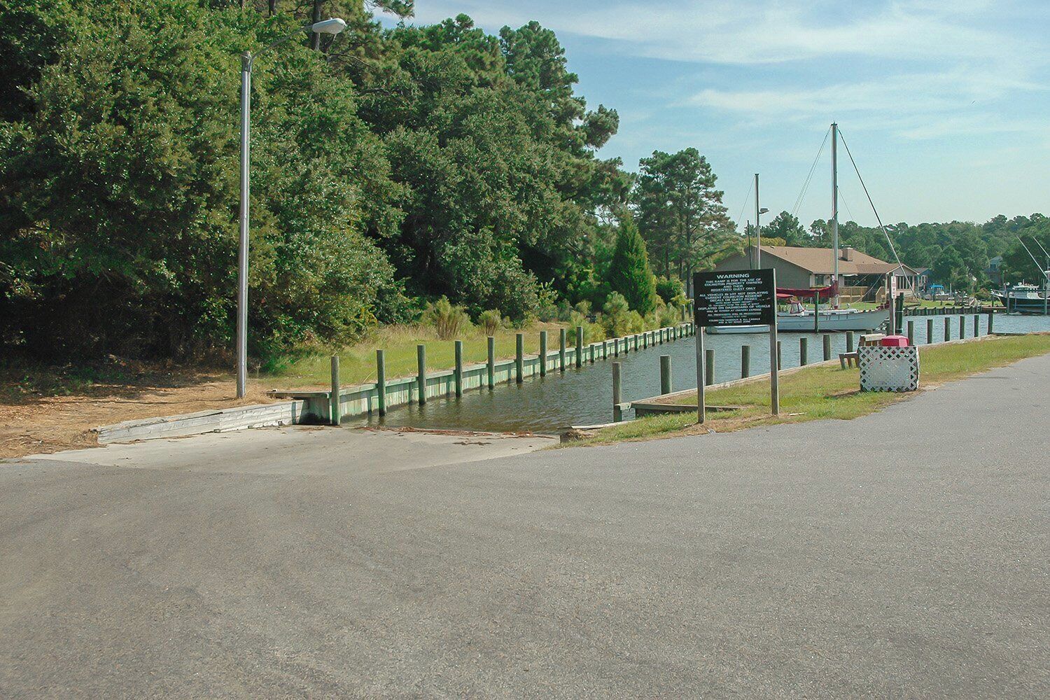 Une route longeant le bord de l’eau, avec un canal, un panneau d’avertissement et un petit bâtiment doté d’un toit.