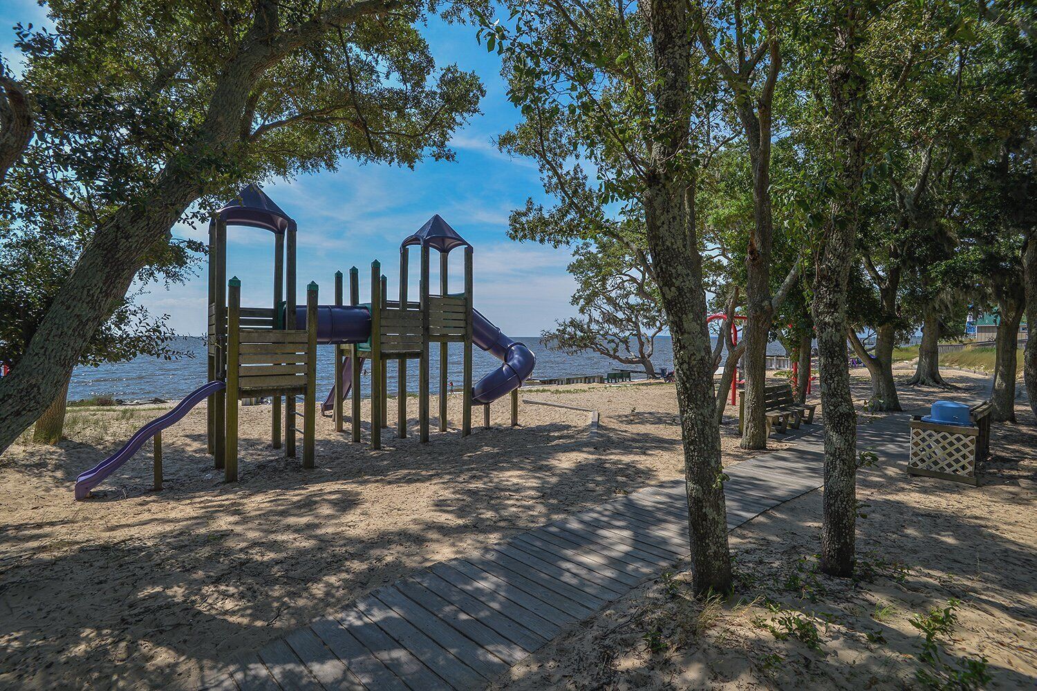 Un parque infantil con toboganes y estructuras para escalar, rodeado de árboles y una zona de arena.