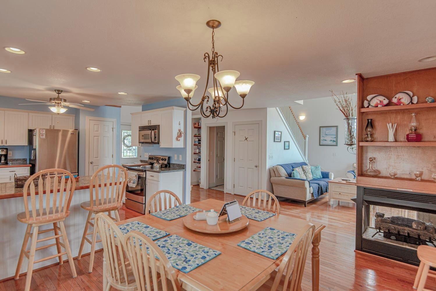 A spacious kitchen with a dining area, wooden chairs, a chandelier, and a fireplace.