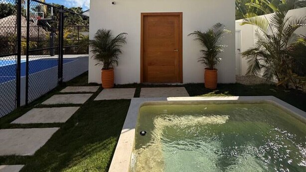 Un bâtiment à deux étages avec une porte en bois, un balcon doté d’une balustrade et une piscine en premier plan.