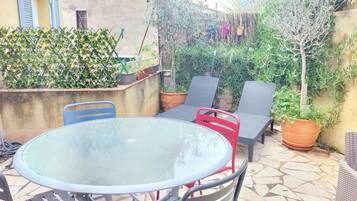 Une terrasse extérieure avec une table ronde en verre, deux chaises et des plantes en pot.