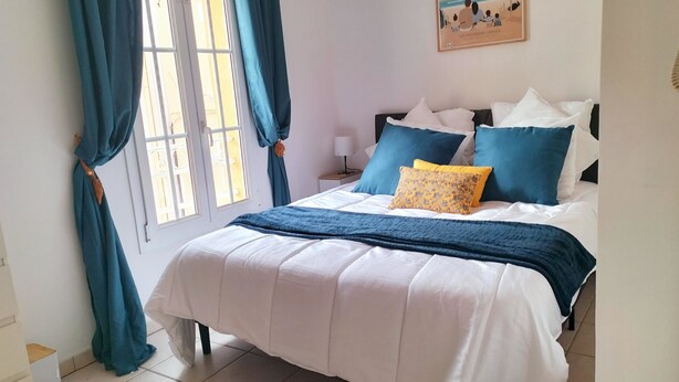 Ein Schlafzimmer mit einem Bett, Vorhängen, einem Nachttisch, einer Lampe und einem Wandbild.