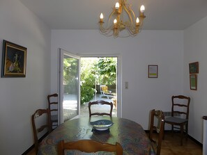 Een eetgedeelte met een ronde tafel, stoelen, een kroonluchter en een deur naar een buitenruimte.