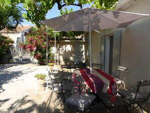 Een terras buiten met een tafel, stoelen, een grote parasol en een bloempot.