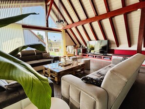 Een ruime woonkamer met een hoge plafond, een televisie en een groot raam.