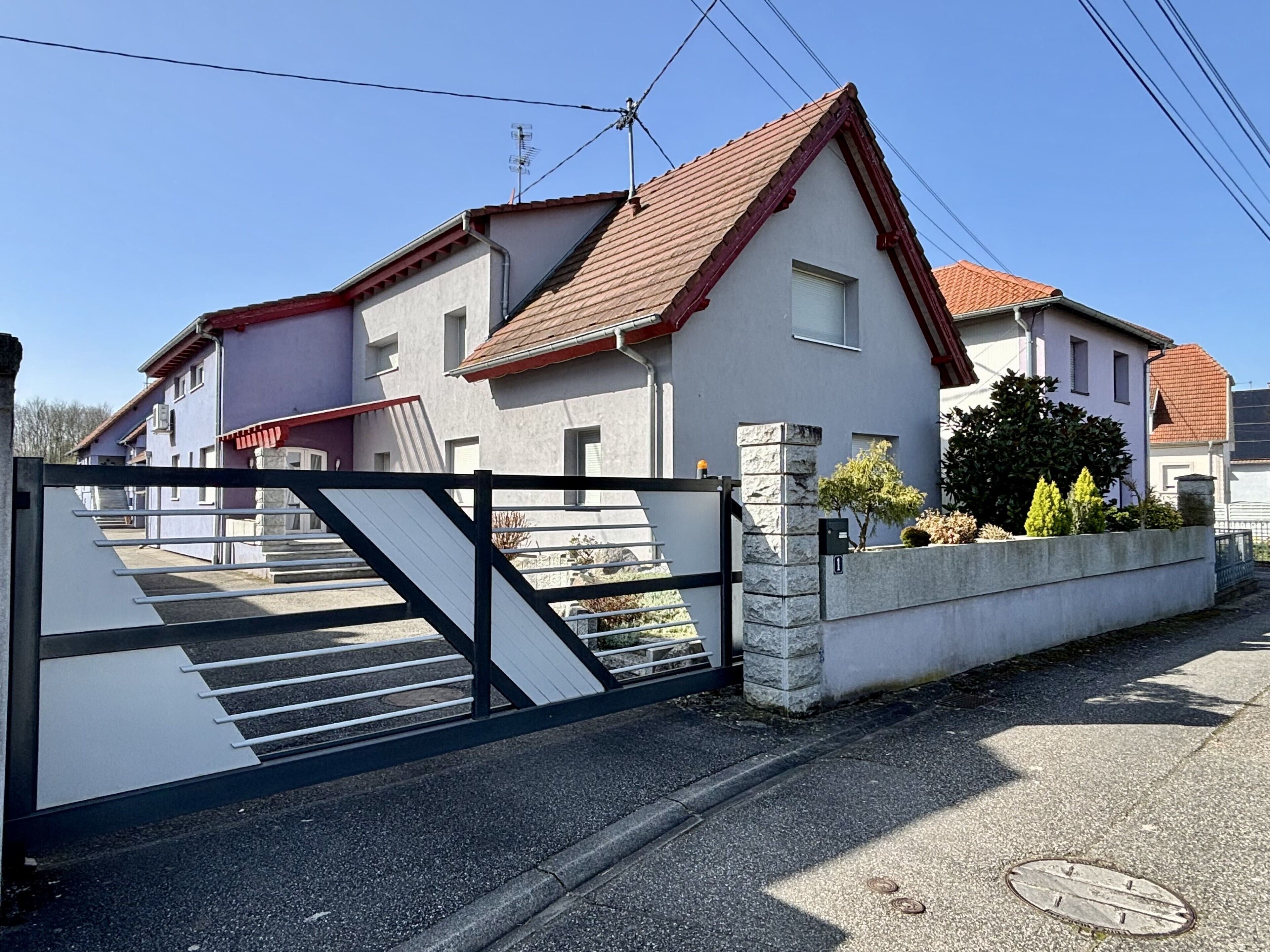 A residential building with a gated entrance, a staircase leading to the entrance, and a stone wall with a mailbox.