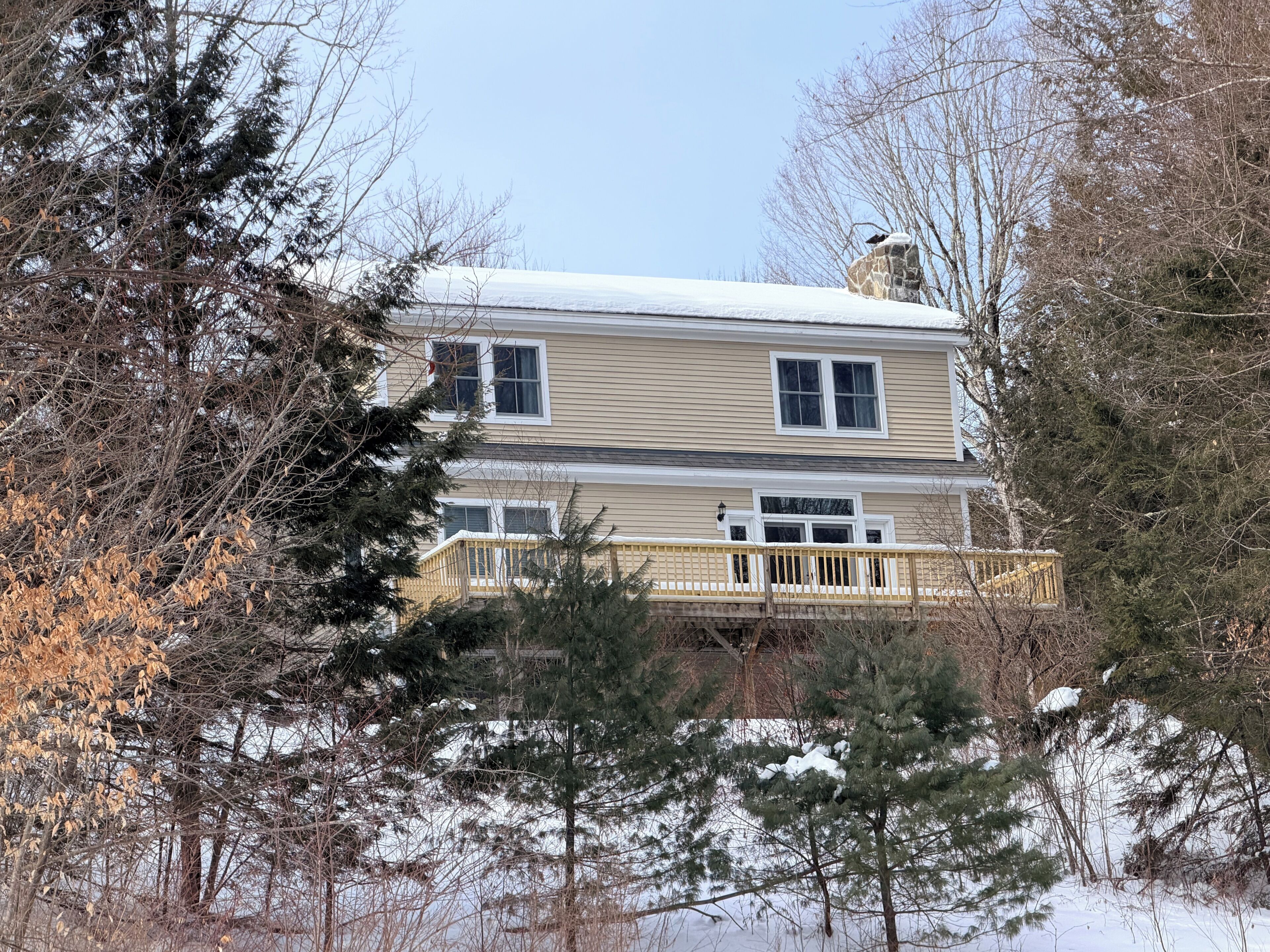 A two-story house with a balcony, surrounded by trees and snow.