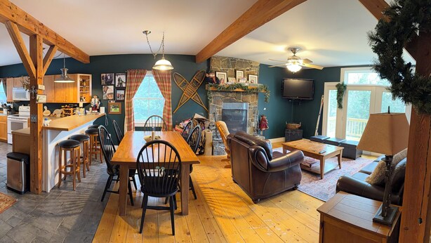 A spacious living area with a fireplace, wooden beams, a dining table with chairs, and a cozy seating area. - Lovely 5-bedroom house in Londonderry perfect for your getaway (Londonderry)