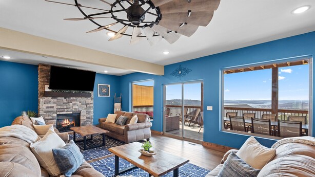 A living room with a fireplace, a ceiling fan, a large window, and a balcony with outdoor furniture.